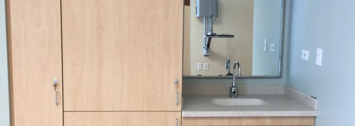 Inside of a healthcare facility, depicting a sink, mirror, and cabinets